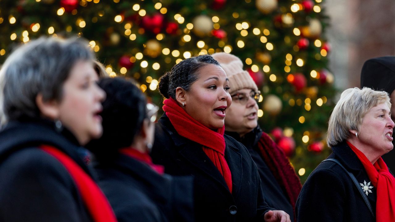 Festive carolers singing beside a brightly lit Christmas tree at an Asheville holiday event.