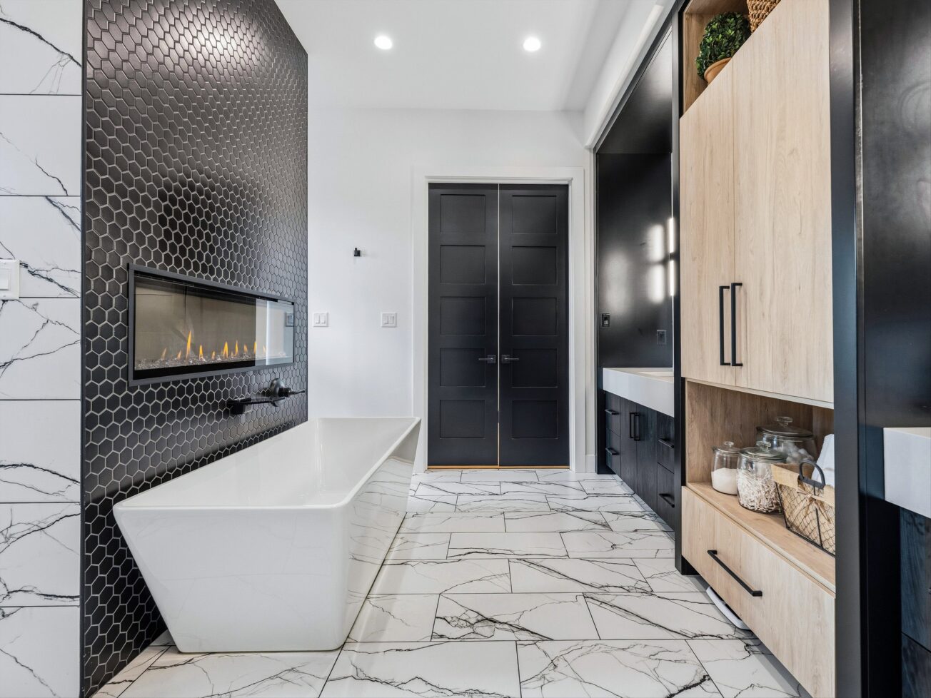 Large, modern bathroom with bathtub under black tiled wall.